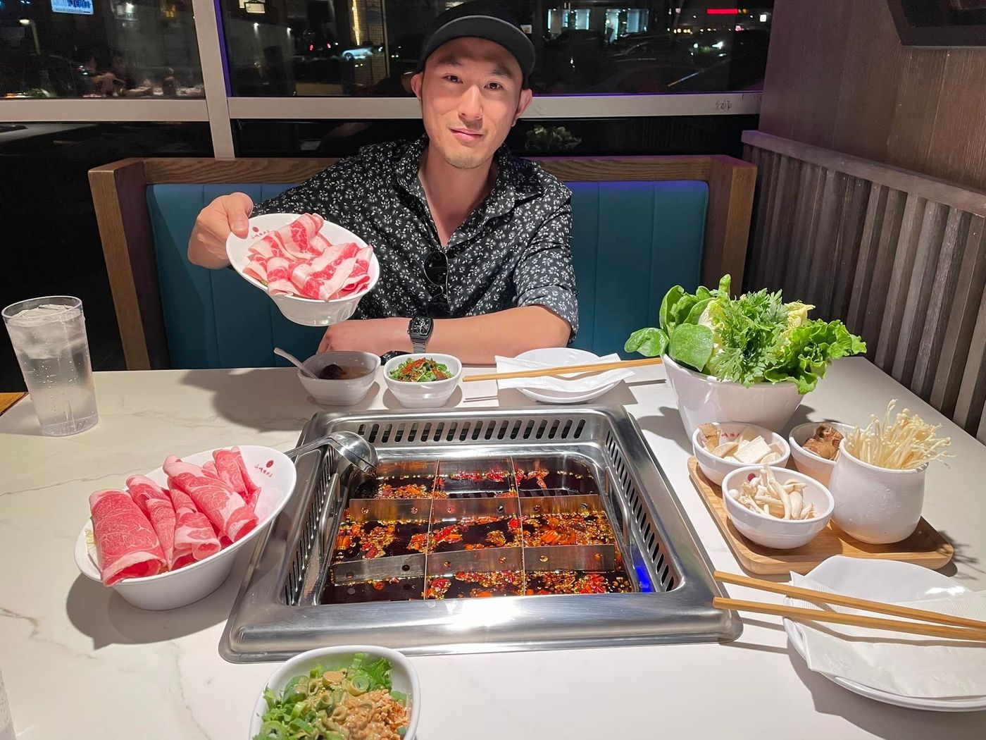 Roger at a hotpot table offering a bowl of sliced beef over a spicy divided broth